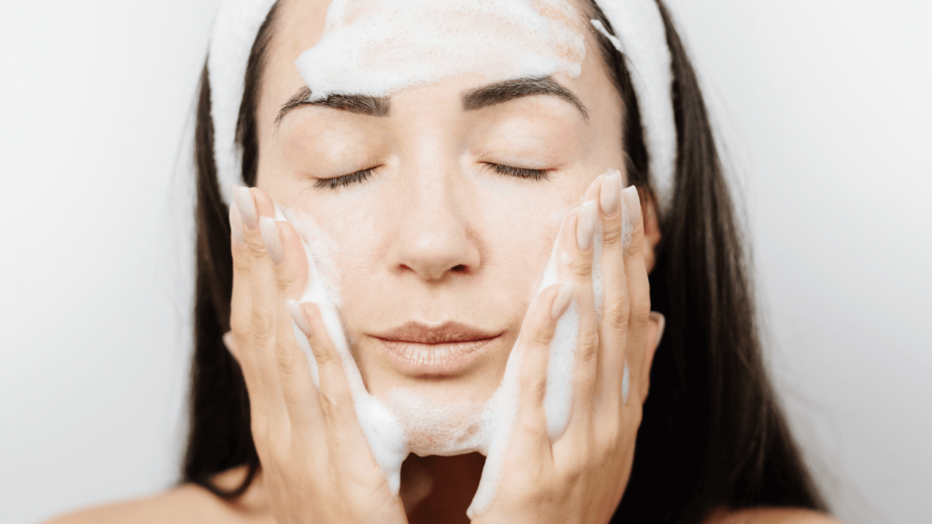 Primer plano de mujer limpiándose la cara con un limpiador facial